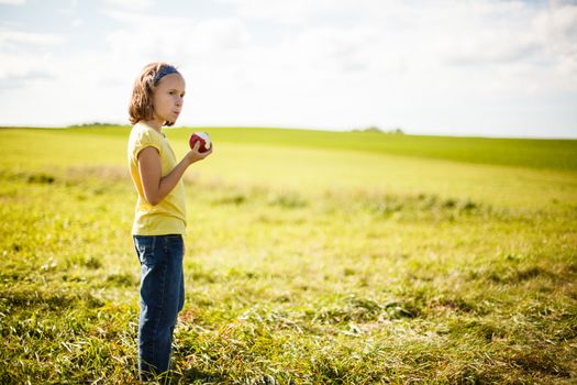 Girl eating an apple in a field near an orchard