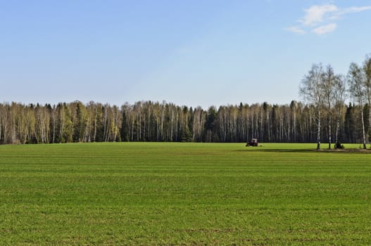 Green field with working tractor in spring time