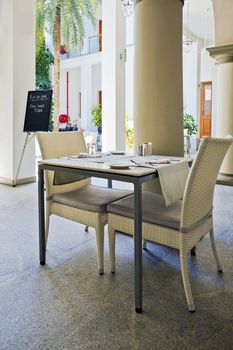 Vertical color portrait of layout by kind permission at the Shanti Restaurant Pondicherry on the patio and garden. A table set for two with blackboard easel announcing the Plat du Jour of Rare done Tuna