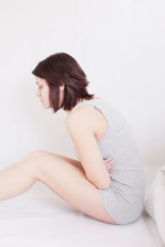 young woman with stomach pain sitting on floor holding holding her tummy