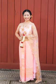 Asian Thai woman/bride in Thai wedding suit is holding flowered garland.