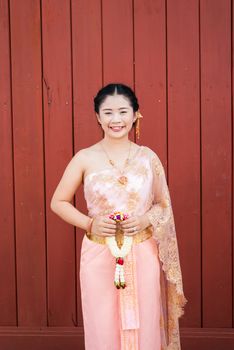 Asian Thai woman/bride in Thai wedding suit is holding flowered garland.