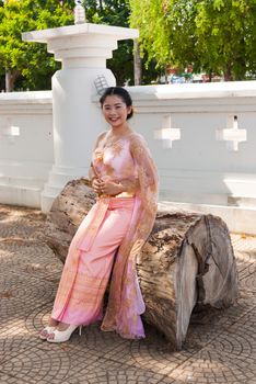 Asian Thai woman/bride in Thai wedding suit is sitting in the wood log.