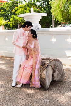 Asian Thai groom is kissing his bride's forehead in smiling face.