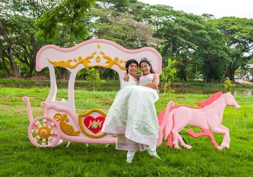 Asian Thai groom is carrying his cute bride in front of romantic carriage with love theme as the Prince and Princess.
