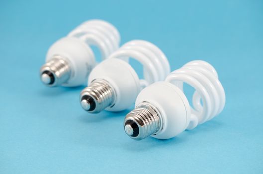 three new novel fluorescent light bulbs on blue background. modern technology use less electricity energy consumption.