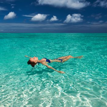 Woman in bikini lying on water at tropical beach