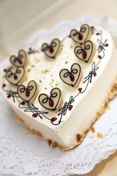 Delicious heart shaped cake with ornamental piping and small hearts on top, closeup view with shalow dof