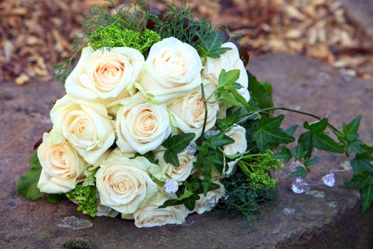 Bridal bouquet of fresh cream coloured roses with a pale apricot centre lying on a stone wall outdoors