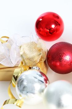 Gold wrapped gift with shiny red and silver Christmas baubles and a decorative bow in a seasonal background