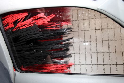 View through the side window from inside a car in a car wash with the rollers rotating on the bodywork