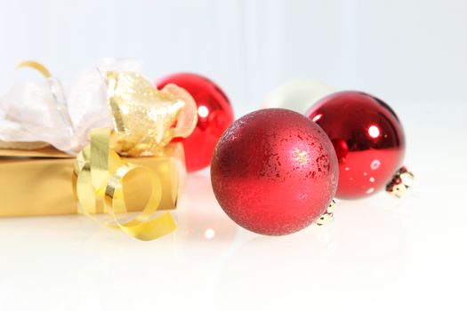 Red Christmas balls and a luxury gift wrapped in gold foil paper and decorated with ornamental bows on a white background