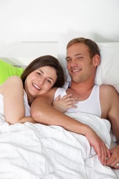 Happy young couple in bed lying close together snuggling and smiling at the camera