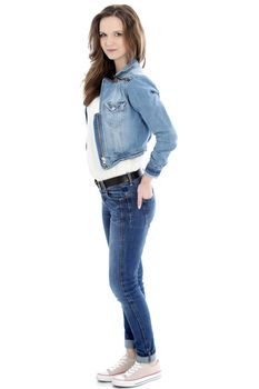 Pretty female student in a denim ensemble of jeans and a jacket standing relaxing with her hands in her pockets looking at the camera isolated on white