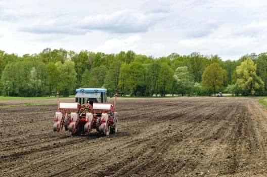 Farmer with tractor planting corn seeds on a field.