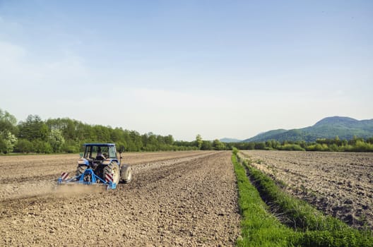 Farmer in blue tractor plowing field surrounded by forests.