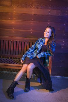 Portrait of a Pretty Mixed Race Young Adult Woman Sitting on Wooden Bench Against a Lustrous Wood Wall Background.