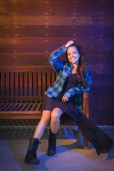Portrait of a Pretty Mixed Race Young Adult Woman Sitting on Wooden Bench Against a Lustrous Wood Wall Background.