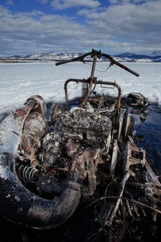 Charred remains of snowmobile burnt out in a winter motorsports mishap on frozen Lake Laberge Yukon Territory Canada