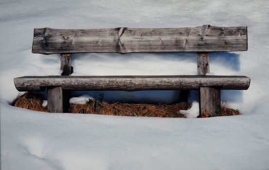 Vacant old rustic wooden bench standing in thick pristine white winter snow