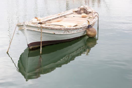 Old white weathered wooden rowing boat or dinghy moored in a harbour in Greece.