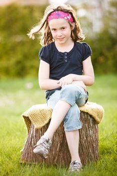 Girl sitting on a tree trunk at the golden hour on a warm summer day