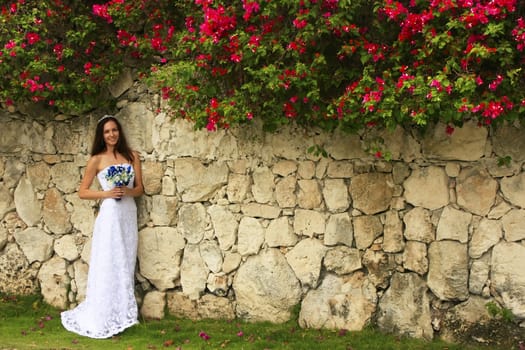 Young woman in wedding dress posing in front of the stone wall with flowers