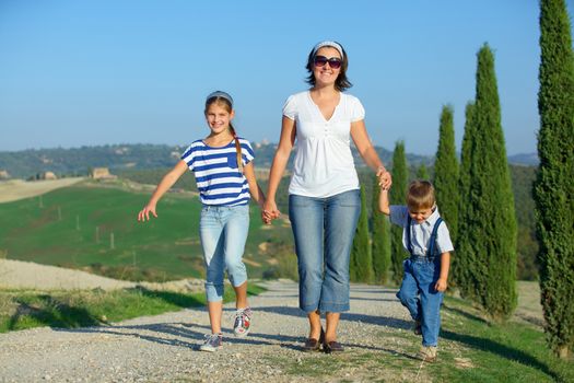 Happy mother with her kids having fun on vacations in Tuscan against cypress alley background