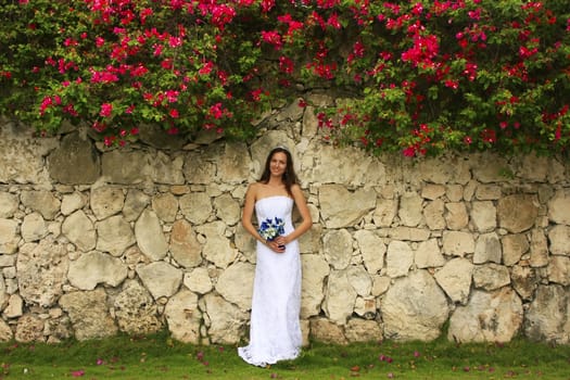 Young woman in wedding dress posing in front of the stone wall with flowers