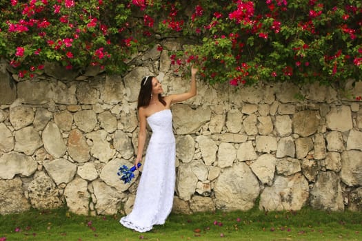 Young woman in wedding dress posing in front of the stone wall with flowers
