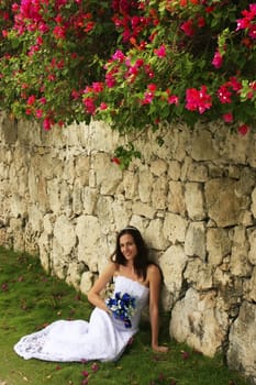 Young woman in wedding dress posing in front of the stone wall with flowers