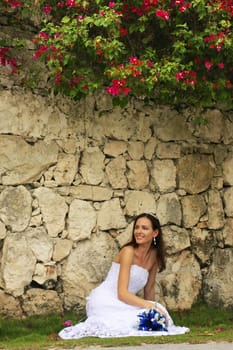 Young woman in wedding dress posing in front of the stone wall with flowers