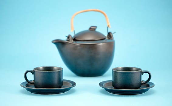 beautiful dishes composition retro black tea pot and small cups in saucers for morning drink on blue background.