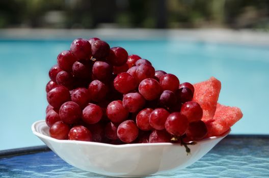 Grapes and watermelon in white plate on table by the swimming pool