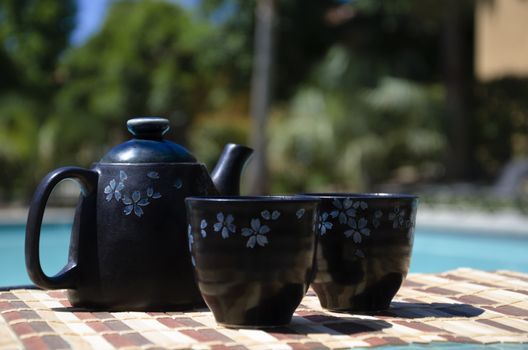 Asian Teapot and two tea cups on table by the swimming pool