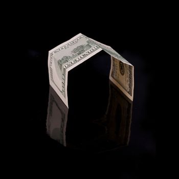 One hundred dollar bill, folded like a house on a black background with reflection