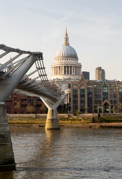 Millenium Bridge frames St Pauls Cathedral in London England at dusk as the sun is setting low in sky.