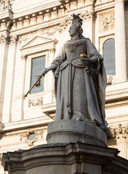 Statue of Queen Anne with bird perched on crown in St Pauls Cathedral in London England at dusk as the sun is setting low in sky.