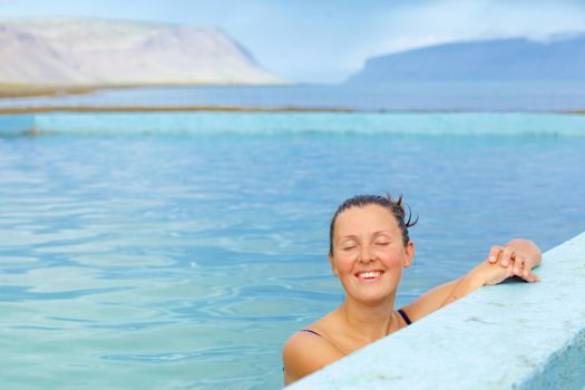 Smiling woman in bathing suit submerged in geothermal mineral pool. Iceland