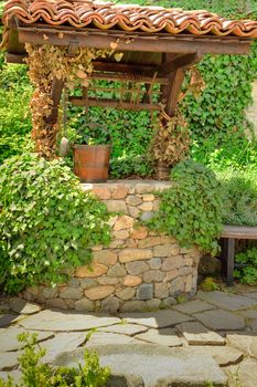 Old water well and a wooden bucket in the garden