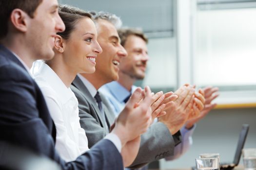 Group of cheerful businesspeople sitting in a row on a presentation and clapping