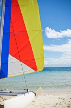 Colourful sail on a catamaran sailboat beached on golden sand facing the tropical ocean