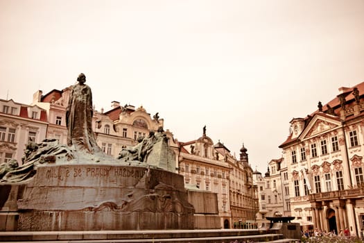 Aged image of central Prague with a low angle view of a figural fountain surrounded by historical buildings and architecture with a pink tone