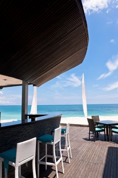 Beautifully situated bar on a wooden deck overlooking the ocean at an upmarket seaside resort in Bali in a travel and tropical summer vacation concept