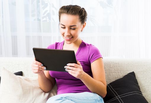 Smiling Brunette girl with dark tablet pc on the sofa