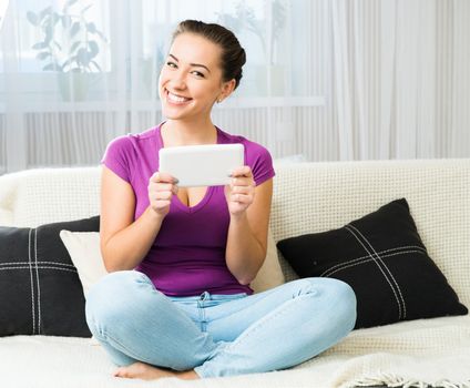 Smiling cute student girl with tablet pc on the sofa