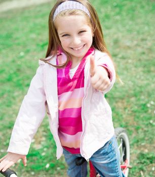 Portrait of Cute smiling little girl on bicycle with thumbs up