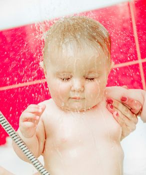 cute smiling baby in bath under a stream of water from the shower