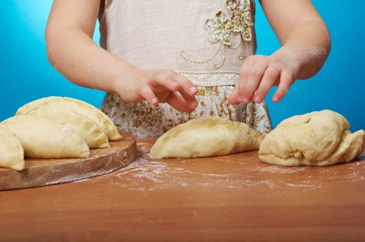 Smiling little girl kneading dough at kitchen .Detail of hands kneading dough