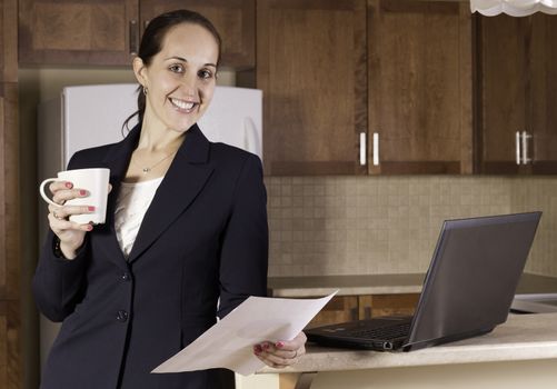 Business woman working on a laptop computer and drinking coffer in her kitchen.